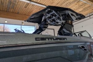 A Centurion boat belonging to the Hemming Family sits indoors, boasting a sleek metallic exterior and a folded canopy structure set against a warm wooden ceiling backdrop.