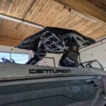 A Centurion boat in a showroom with a partially opened roof mechanism, under a wooden ceiling with fluorescent lights.