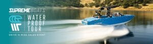A blue Supreme boat speeds across a lake with passengers onboard, showcasing the thrill of the "Supreme Wakeboats Waterproof Tour" Drive-N-Ride Sales Event.