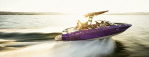 A purple speedboat with four people onboard moves quickly across a sunlit lake, creating a large wake behind it. Interested in adventures like this? Submit a Dealer Application today to become a dealer and bring excitement to your area.