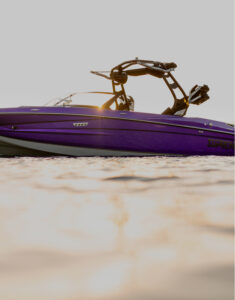 A purple Supreme Wakeboat with black fittings floats on calm water, with the sun shining behind the boat’s frame.