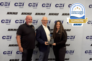 Three people stand before a CSI Award backdrop, the center person proudly holding a glass trophy for excellence. A "Manufacturer Excellence 2025 Supreme NMMA" badge, highlighting Supreme Boats' commitment to customer satisfaction, appears on the right.