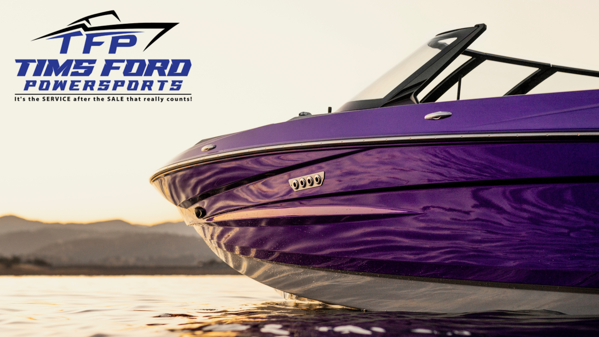 Close-up of a purple powerboat on the water at sunset, with the Tims Ford Powersports logo and slogan in the upper left corner.