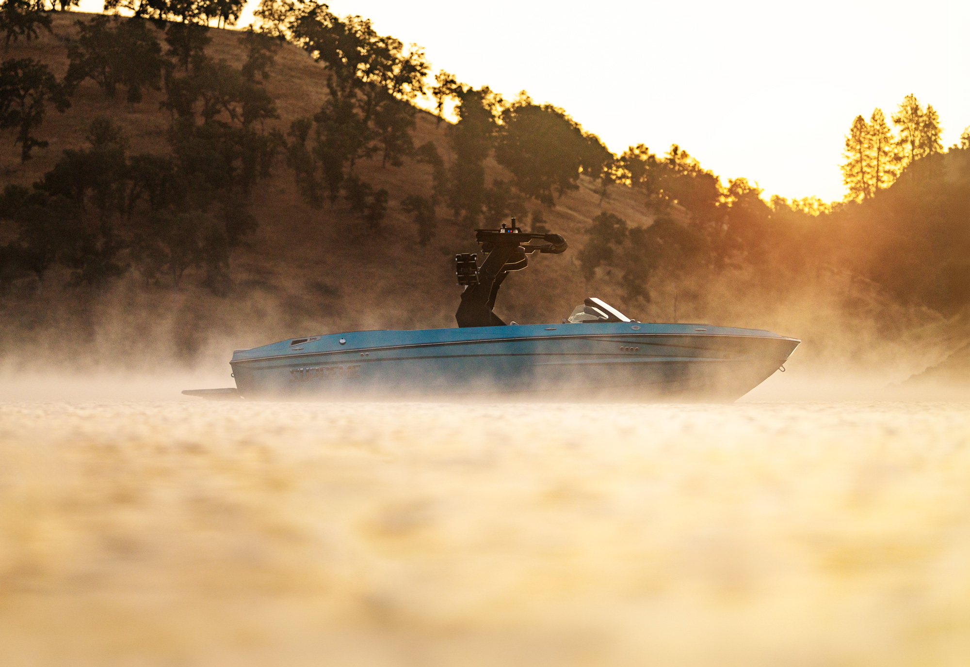 A sleek speedboat travels across a misty lake at sunrise, with hills and trees visible in the background—start your own adventure when you Find a Dealer through our Supreme Dealer Search.