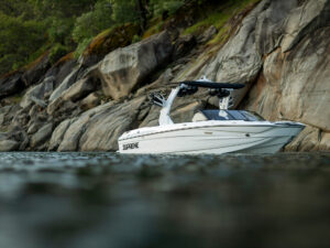 A white motorboat labeled “Supreme” floats near rocky cliffs with green trees visible above the rocks, making it a perfect option for a boat trade in if you’re considering upgrading your current vessel.