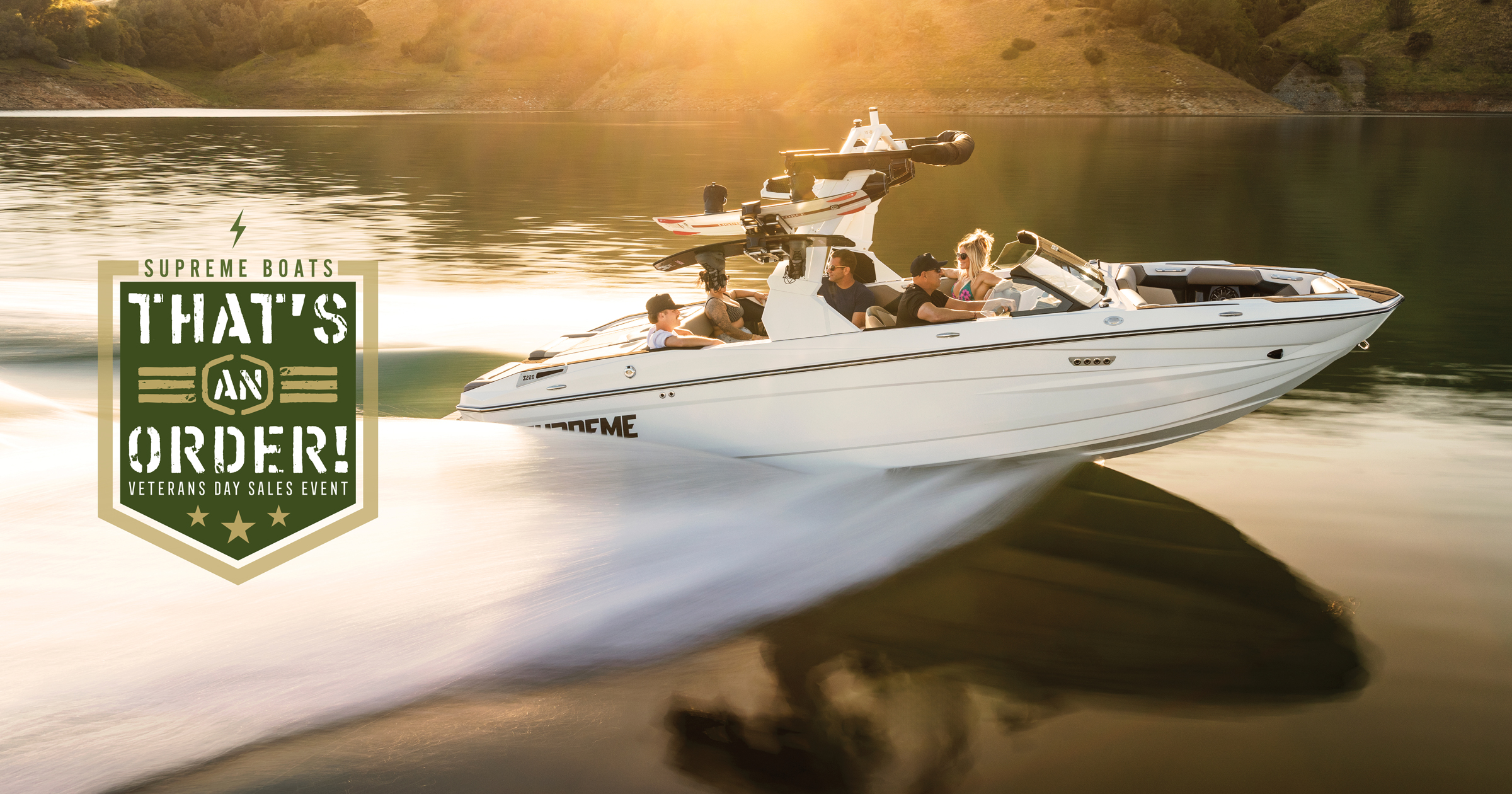 A white speedboat with four people glides quickly across a lake at sunset, highlighting the Supreme “That’s an Order! Veteran’s Day Sales Event” badge on the left.