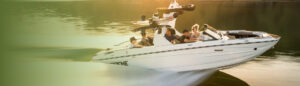 A white Supreme wakeboat with four people onboard moves quickly across calm water at sunset, carrying wakeboards on a tower.